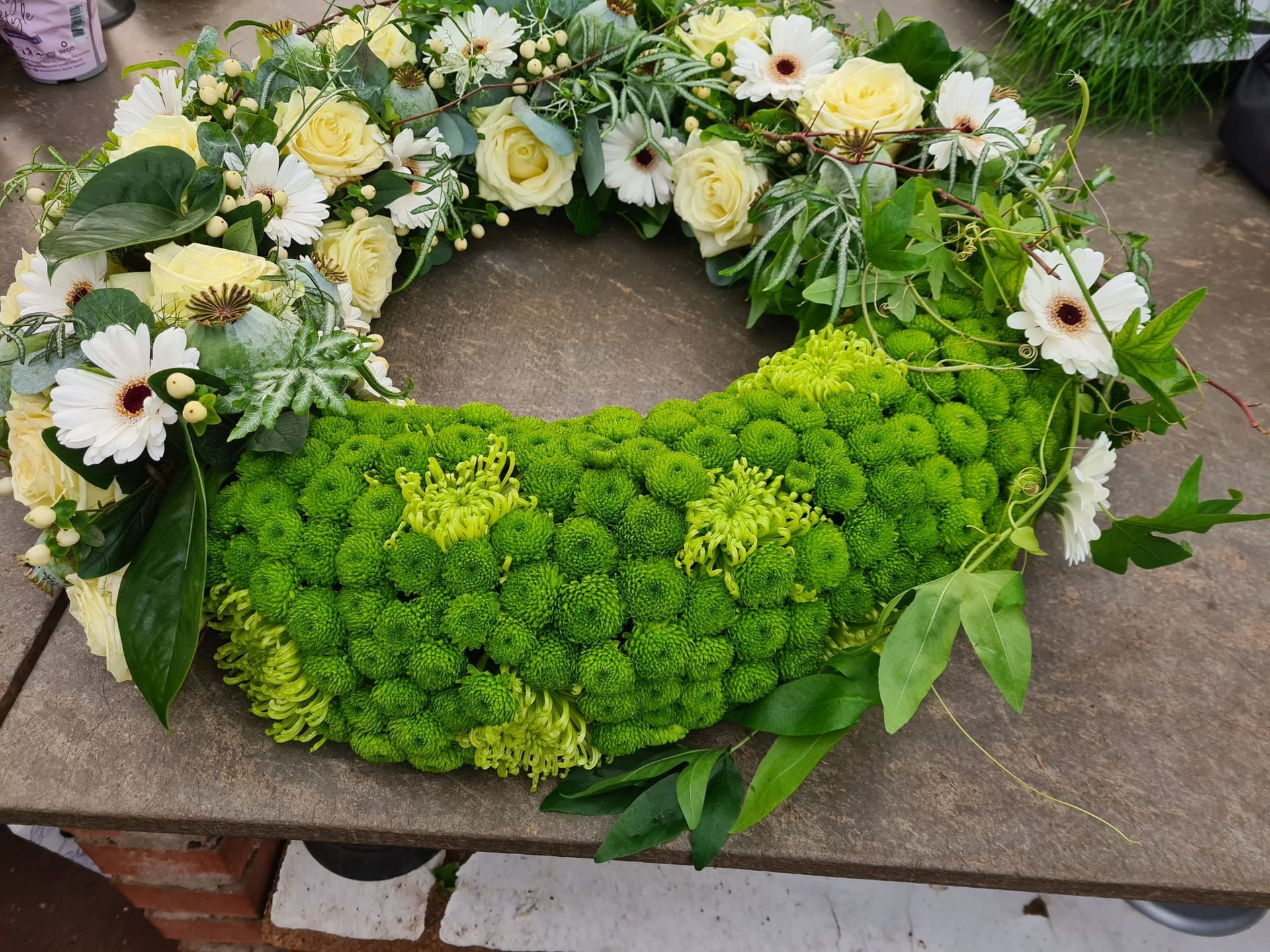Auf einem Tisch steht ein Kranz aus grünen und weißen Blumen.