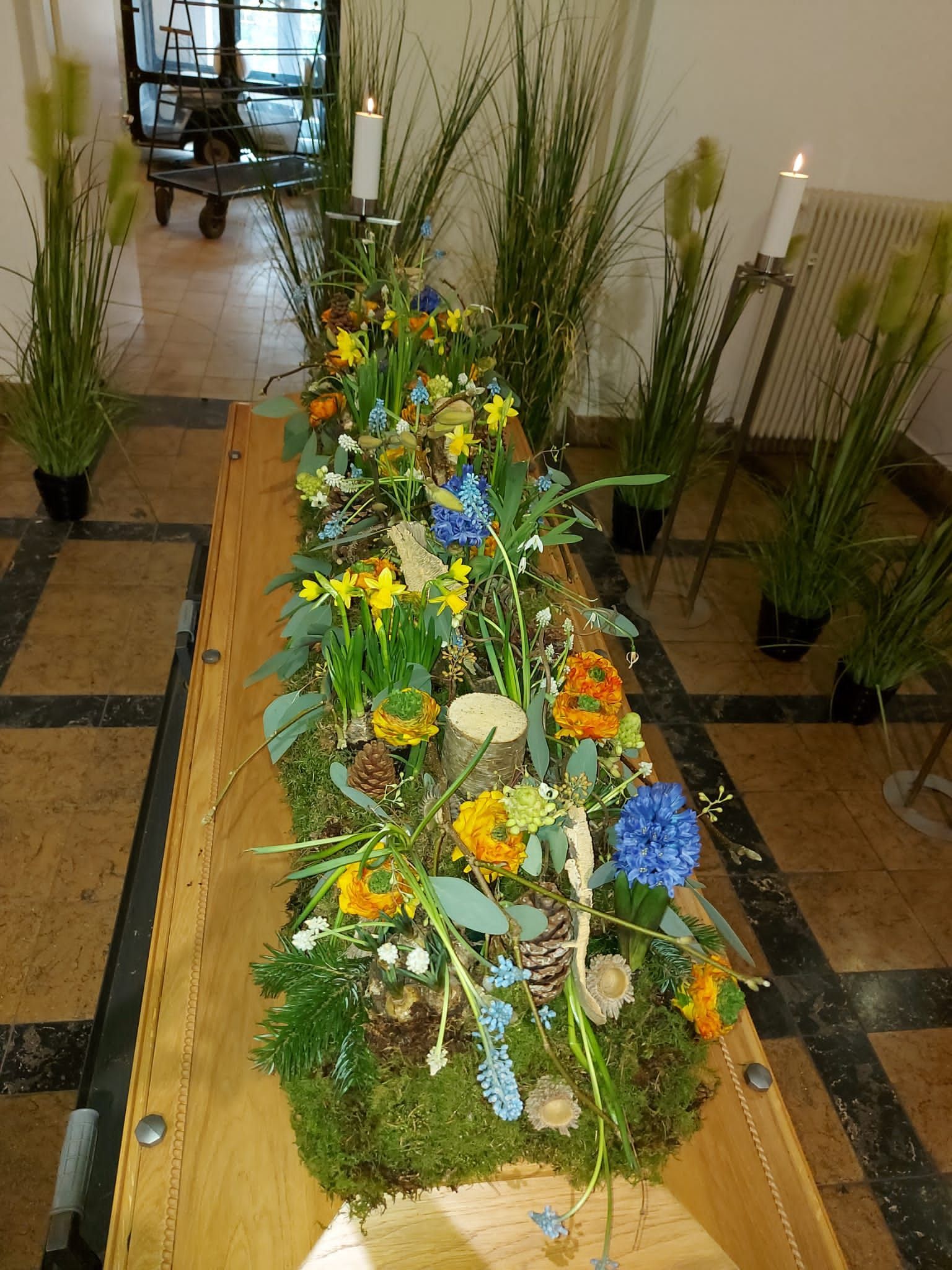 Ein Holzsarg ist mit Blumen und Kerzen geschmückt.