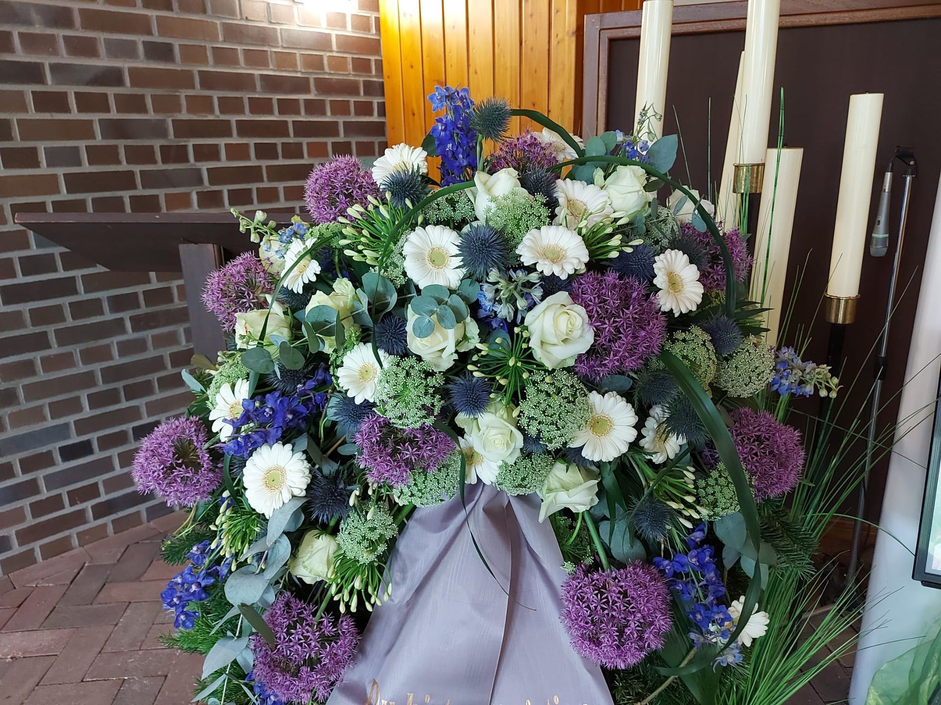 Vor einem Backsteingebäude steht ein großer Strauß violetter und weißer Blumen.