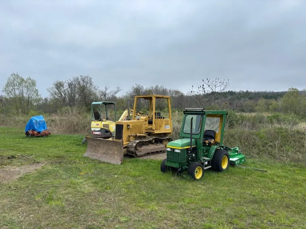 Green and yellow tractors and a bulldozer parked in a grassy field under cloudy skies