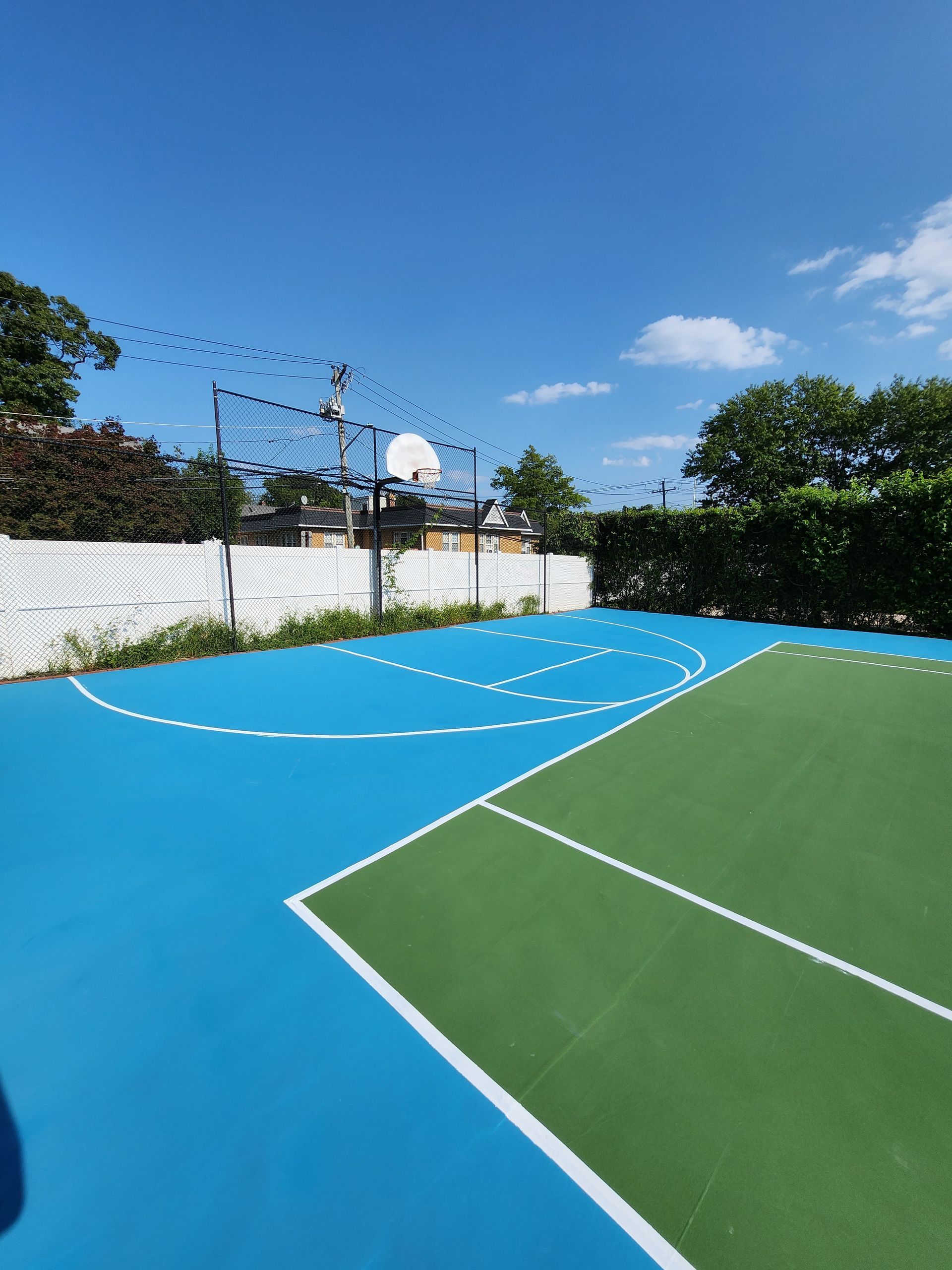 A blue and green basketball court with a fence in the background