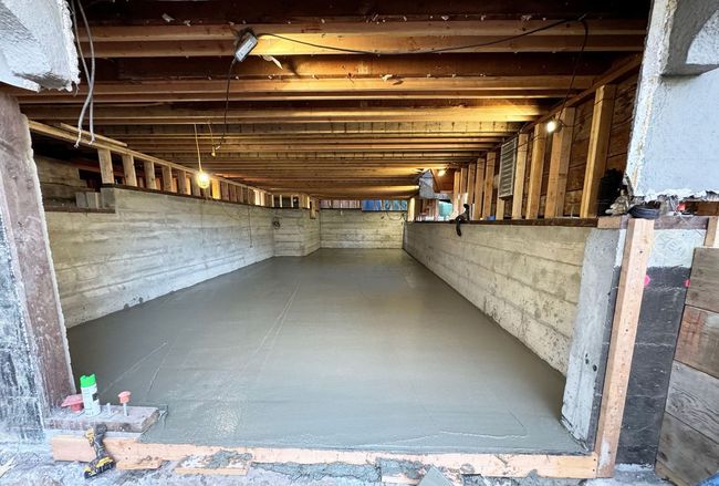 Construction workers pouring and leveling wet concrete into a wooden frame at a building site.