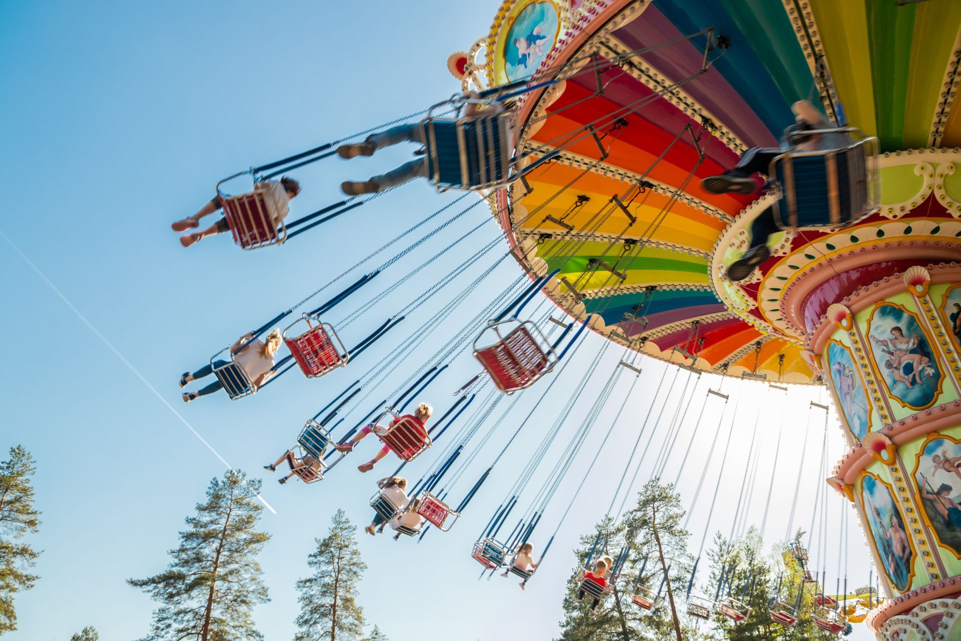 A carousel swing ride with colorful rainbow canopy and riders in motion against a bright blue sky.