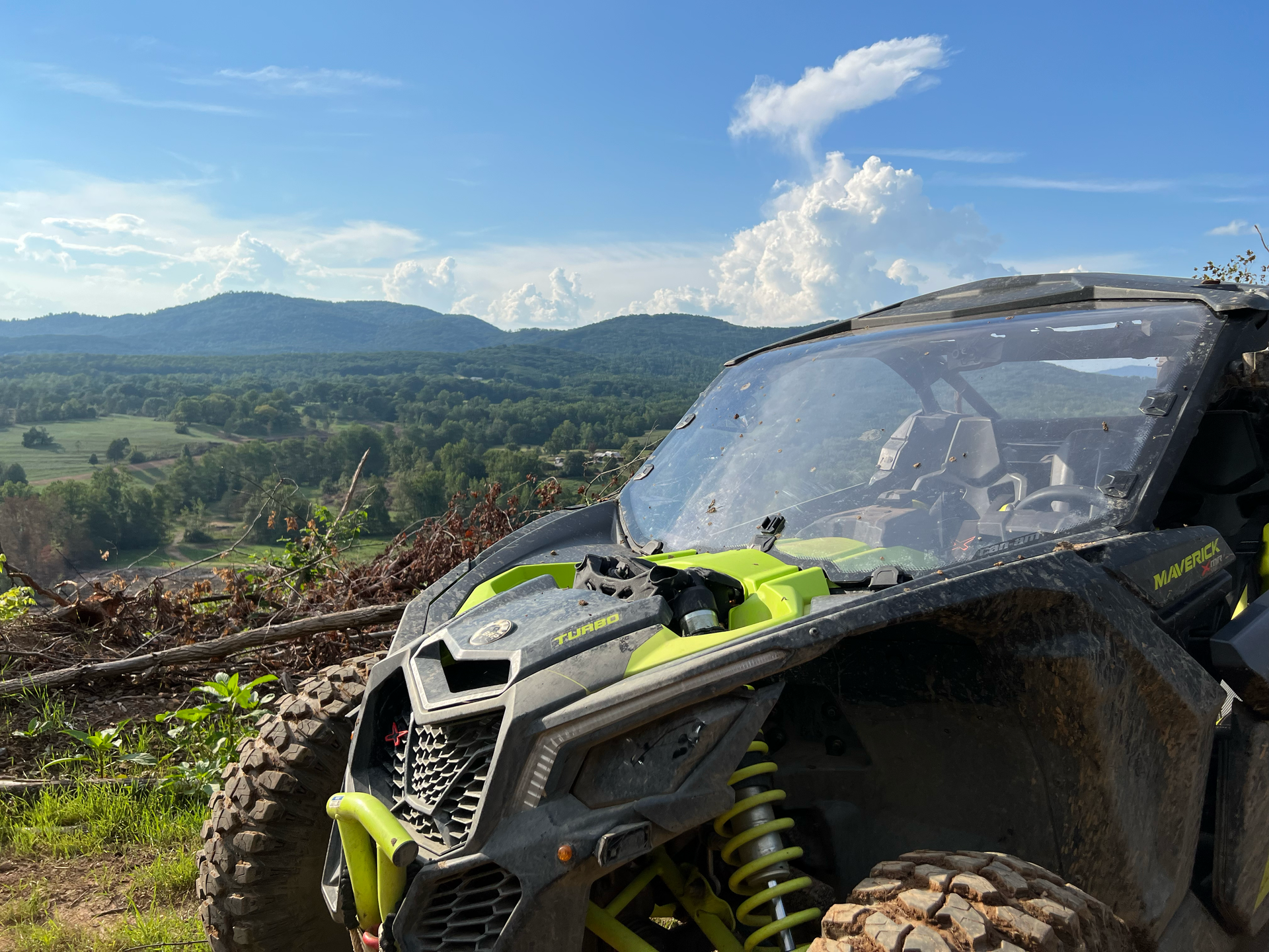 Side-by-side ATV on a hillside overlooking a green valley under a blue sky with fluffy clouds.