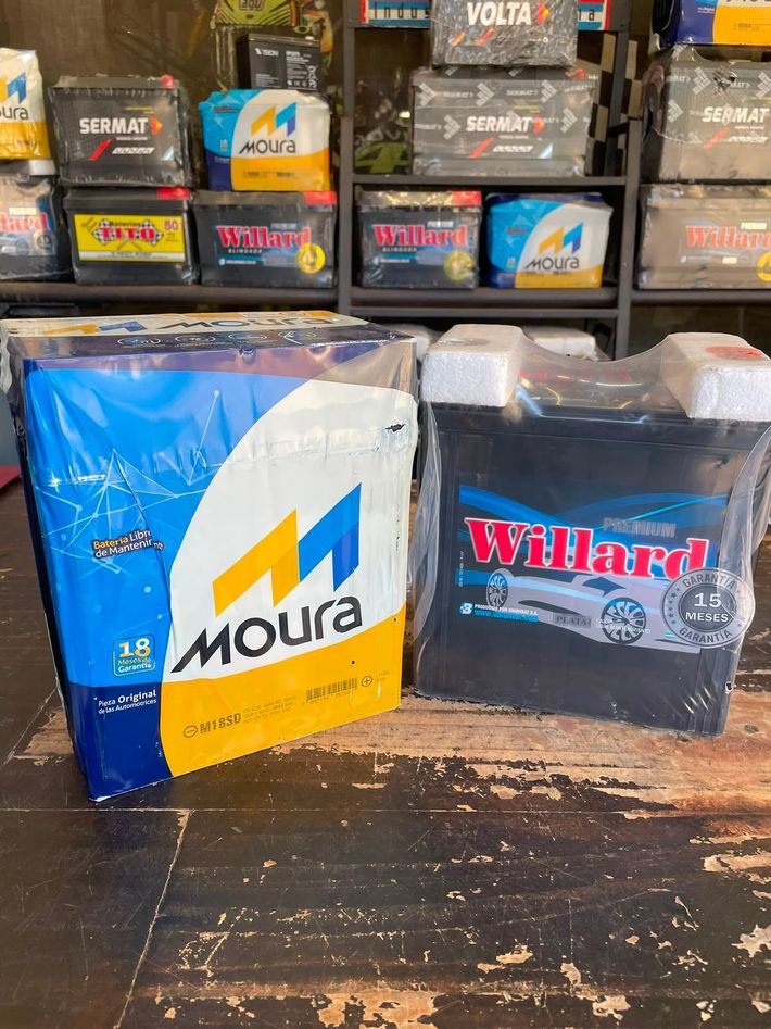 Pilas apiladas en un estante de una tienda, incluyendo cajas de Moura azules y blancas y cajas de Willard negras.