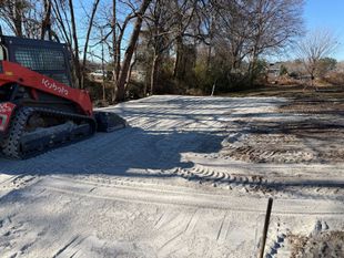 Red skid-steer bulldozer grading a snowy dirt road beside leafless trees.