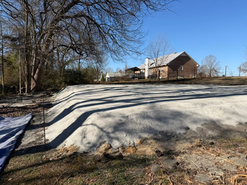 Snow-covered yard with a brick house in the background and long tree shadows across the ground
