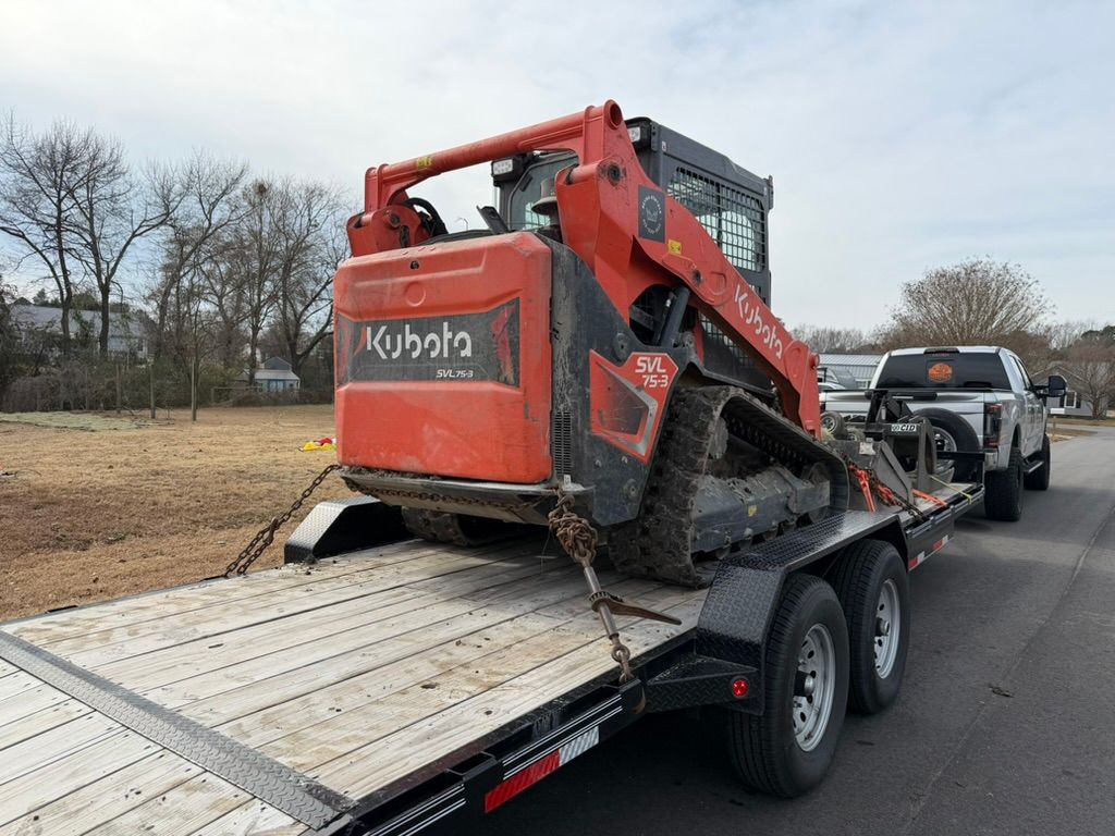 Red skid steer loaded on a tilt trailer being towed on a road