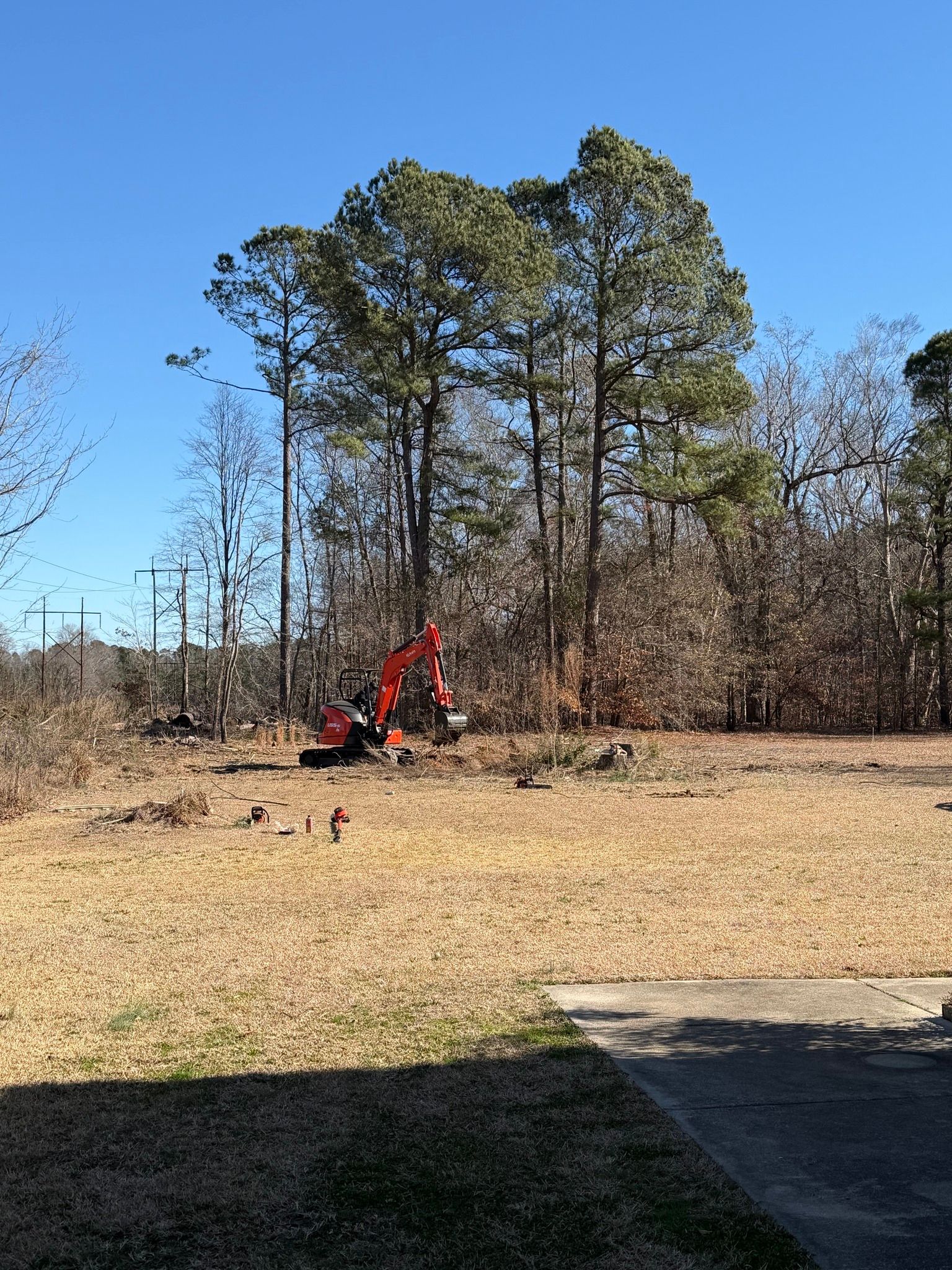 Person using a red excavator in a grassy field beside trees and a paved path
