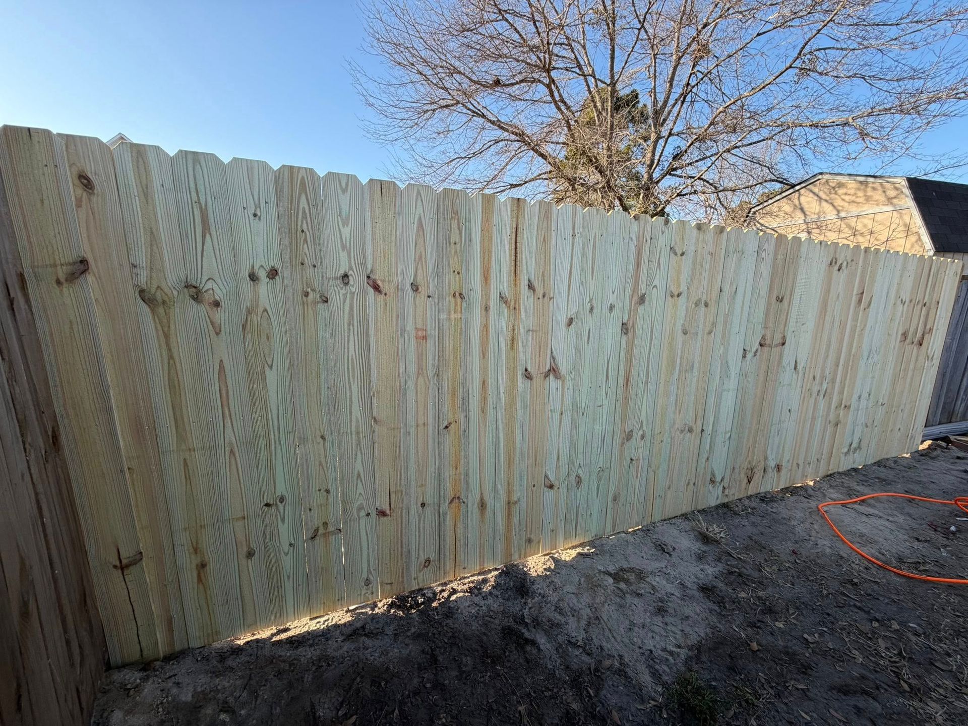 New wooden fence panels in a dirt yard under a clear blue sky