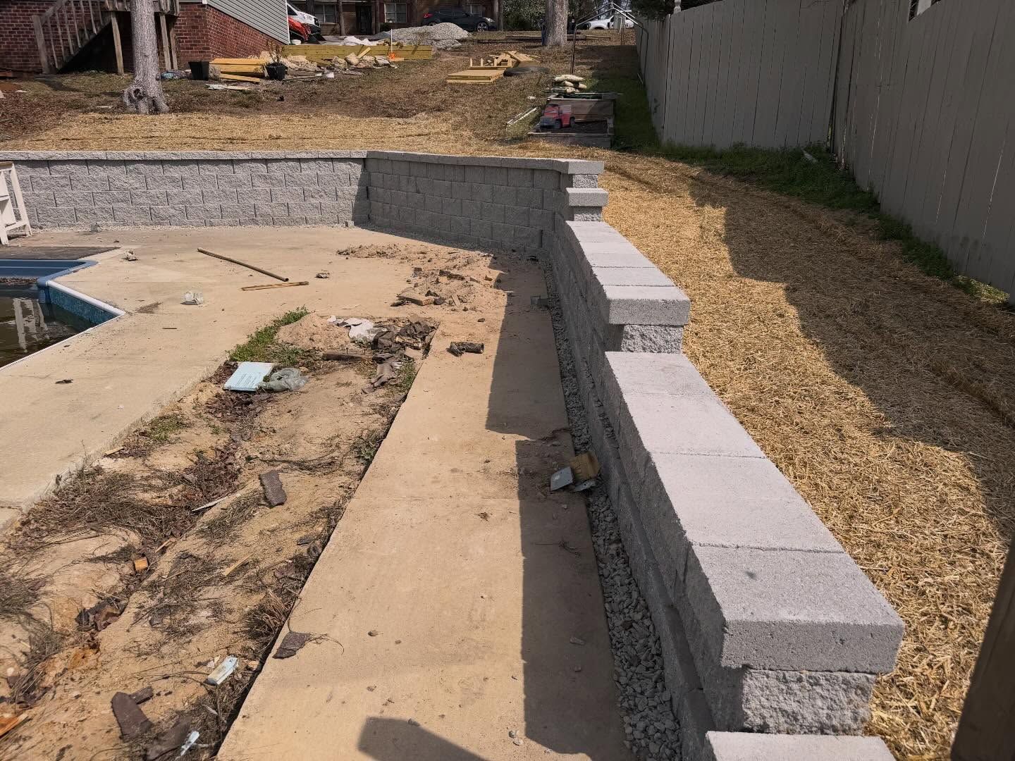 Partially built backyard pool with stacked cinder blocks, gravel, and unfinished concrete deck