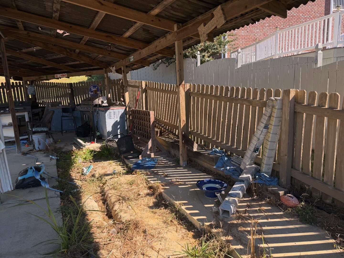 Backyard shed with wooden fence, tools, and scattered equipment in sunlight