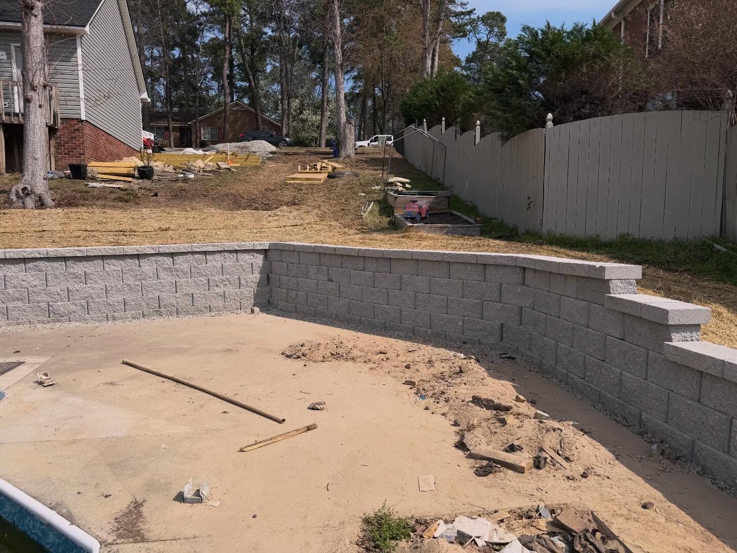 Empty backyard with a curved gray retaining wall around a sandy excavation area.