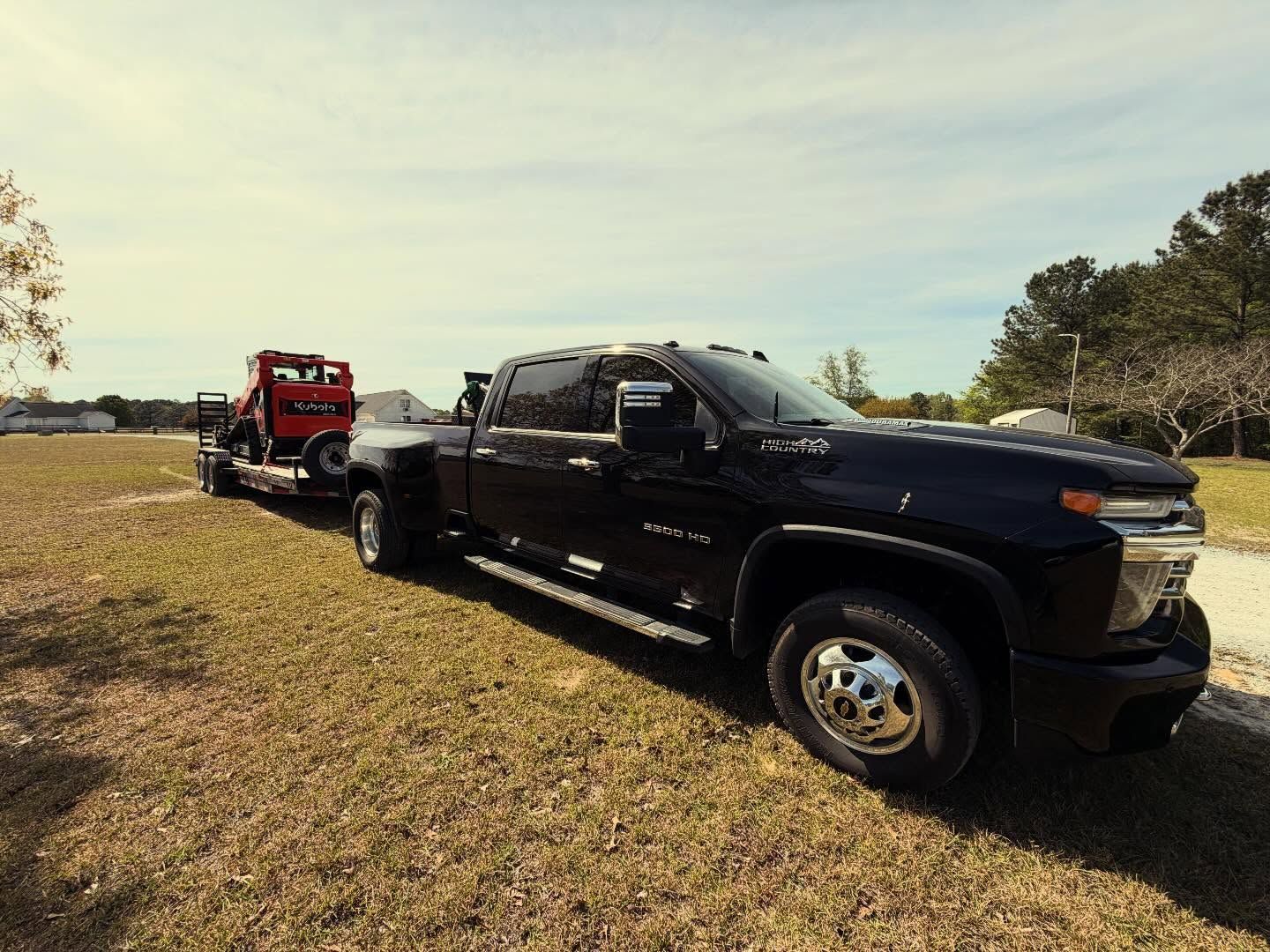 Black pickup truck towing a red trailer across a grassy field under a sunny sky