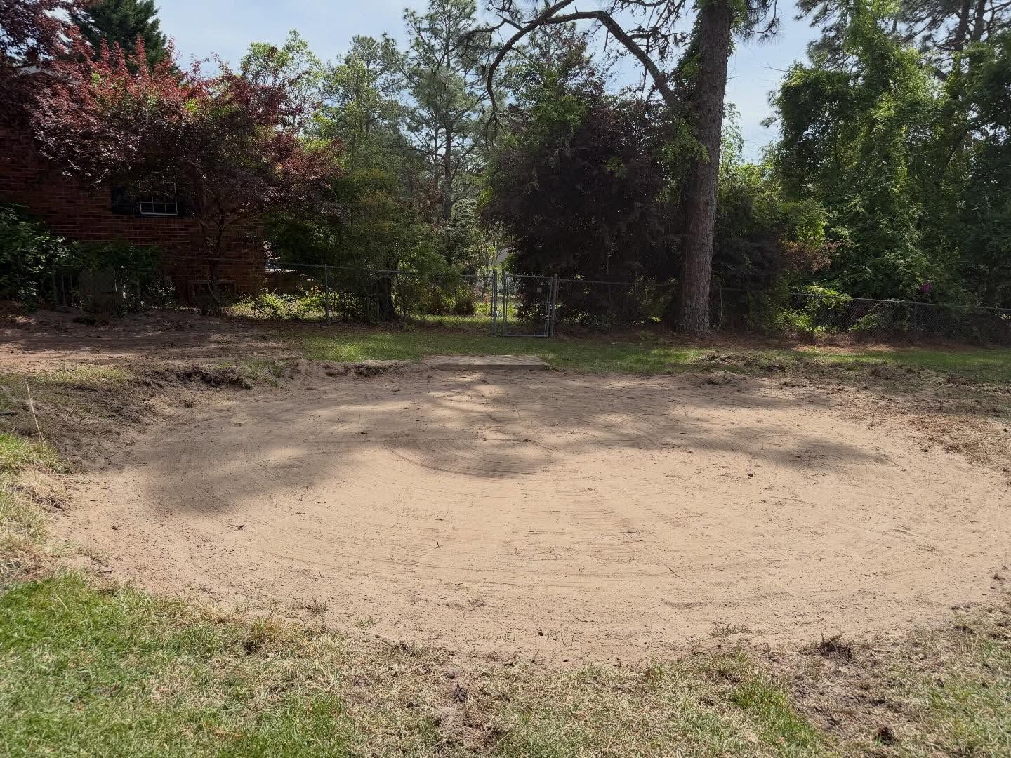 Sandy clearing in a wooded area with trees and shrubs around the edges