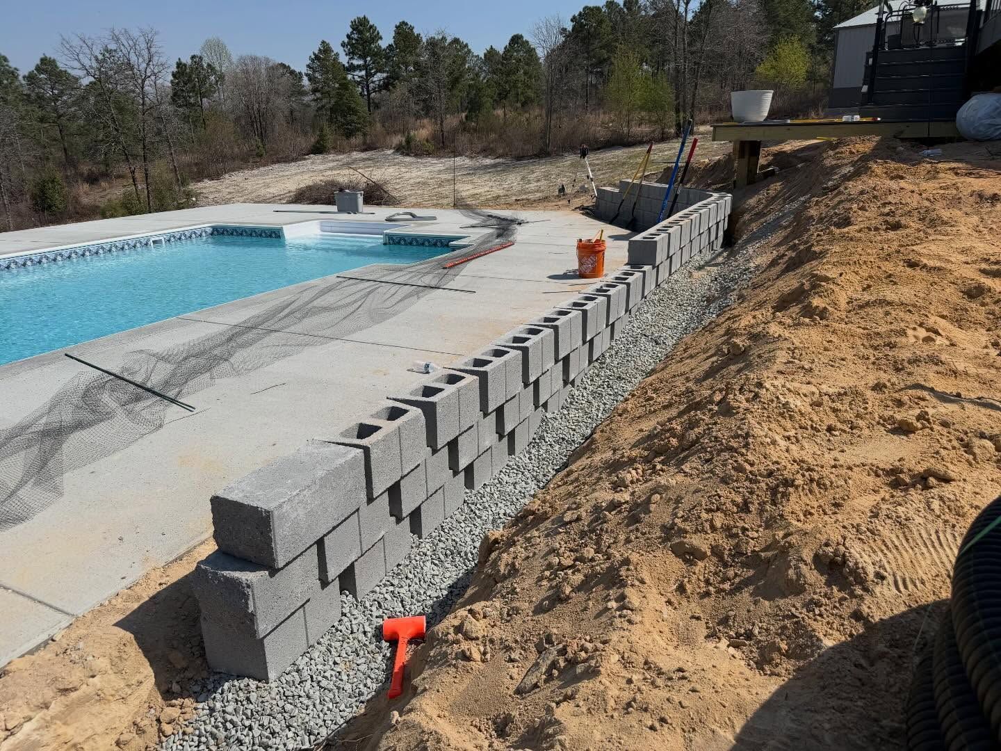 Partially built cinder block retaining wall beside a swimming pool on a dirt slope