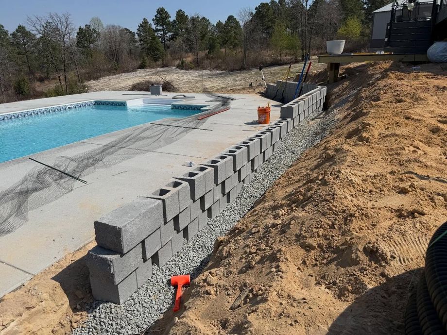 Partially built cinder block retaining wall beside a swimming pool on a dirt slope