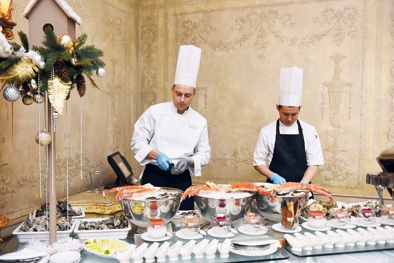 Two chefs at a buffet table, preparing seafood, with a festive holiday decoration.