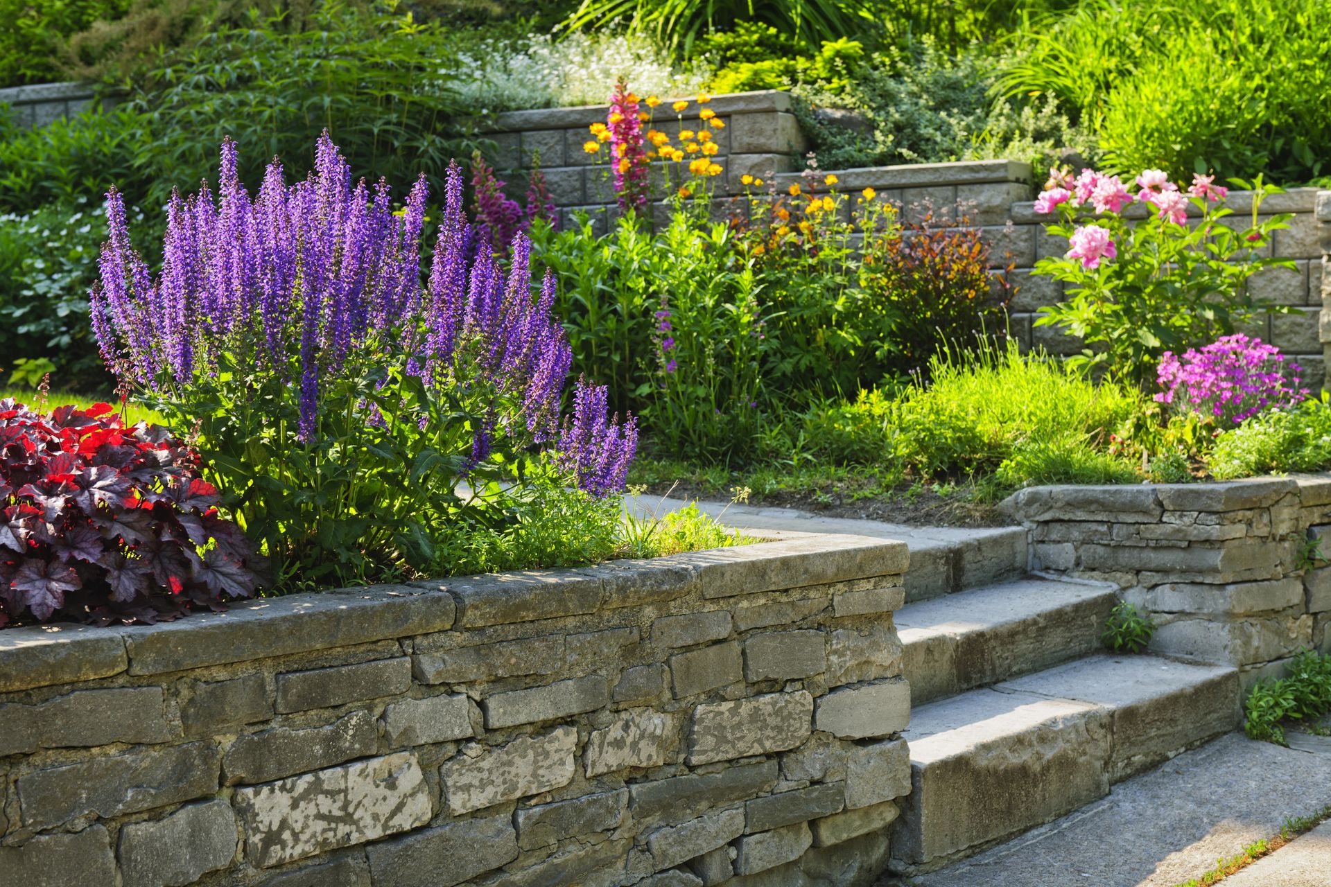 A stone wall surrounds a garden filled with lots of flowers and plants.