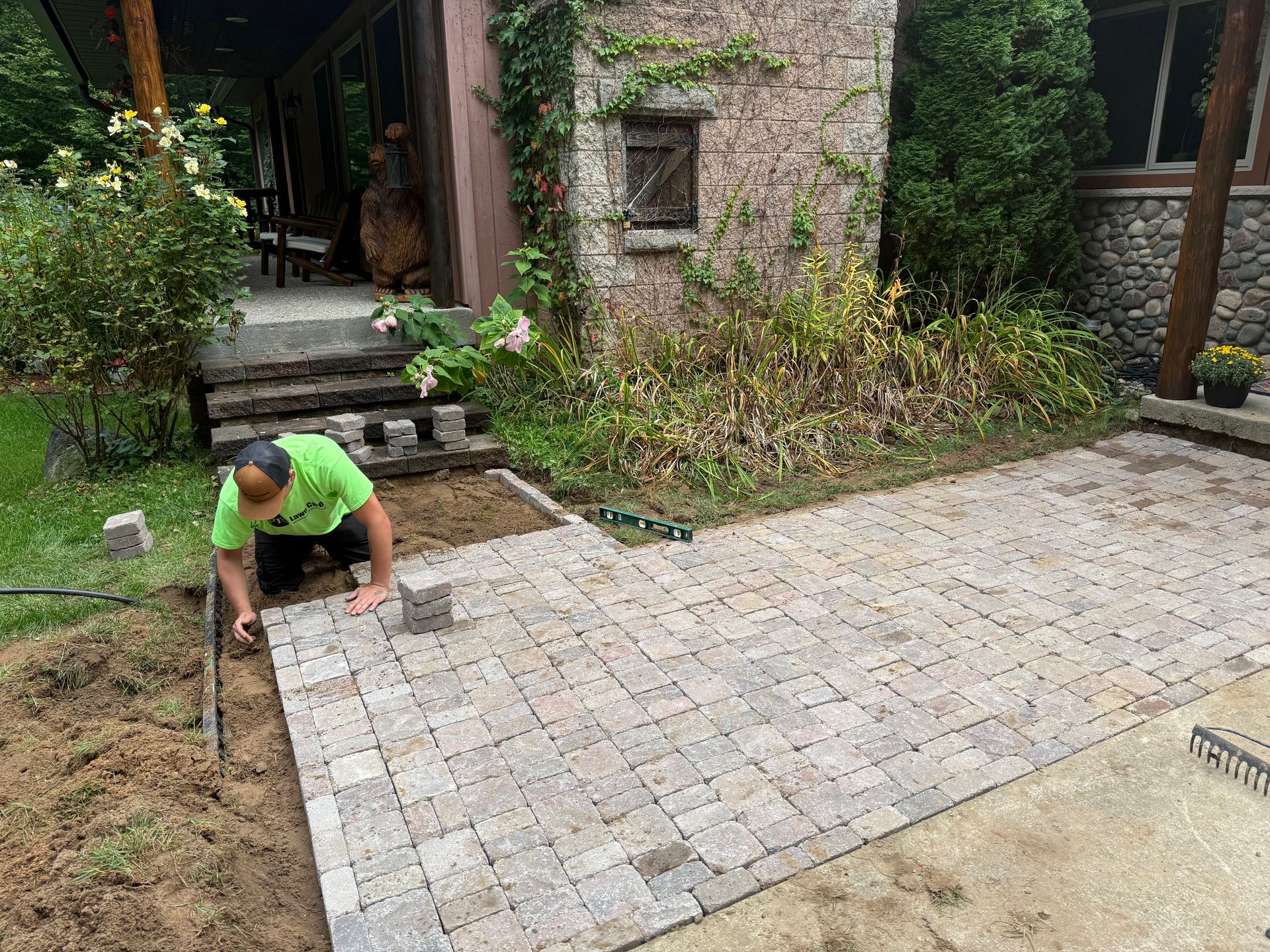 Man laying paving stones on a patio next to a stone building.