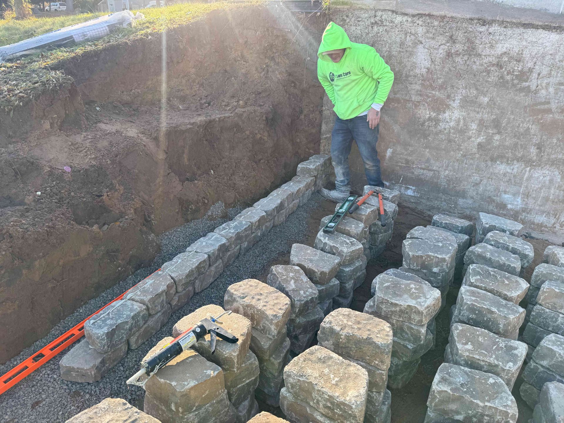 Man in neon green jacket building a stone wall in an outdoor setting.