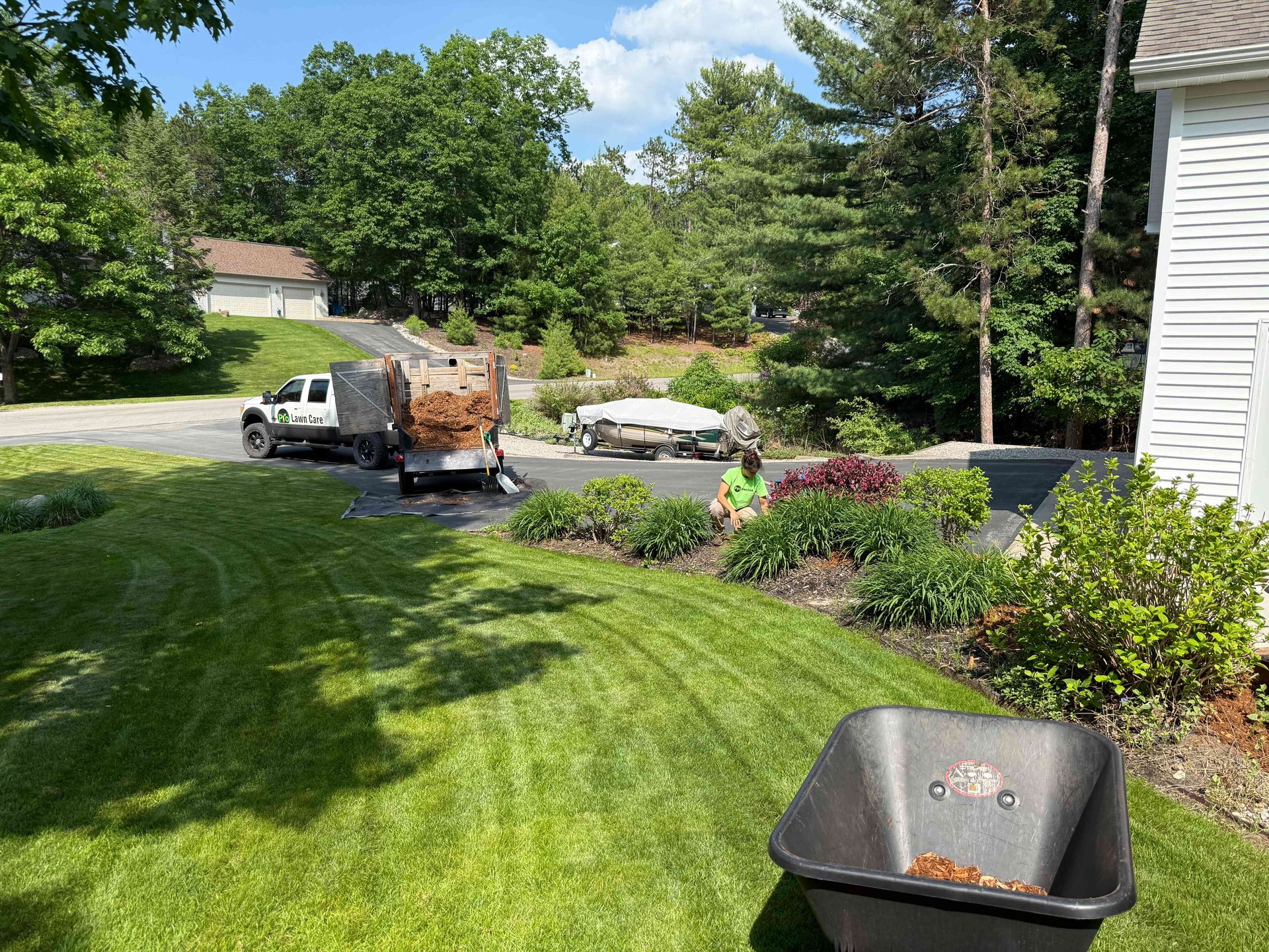 A black wheelbarrow is sitting in the middle of a lush green lawn next to a truck.