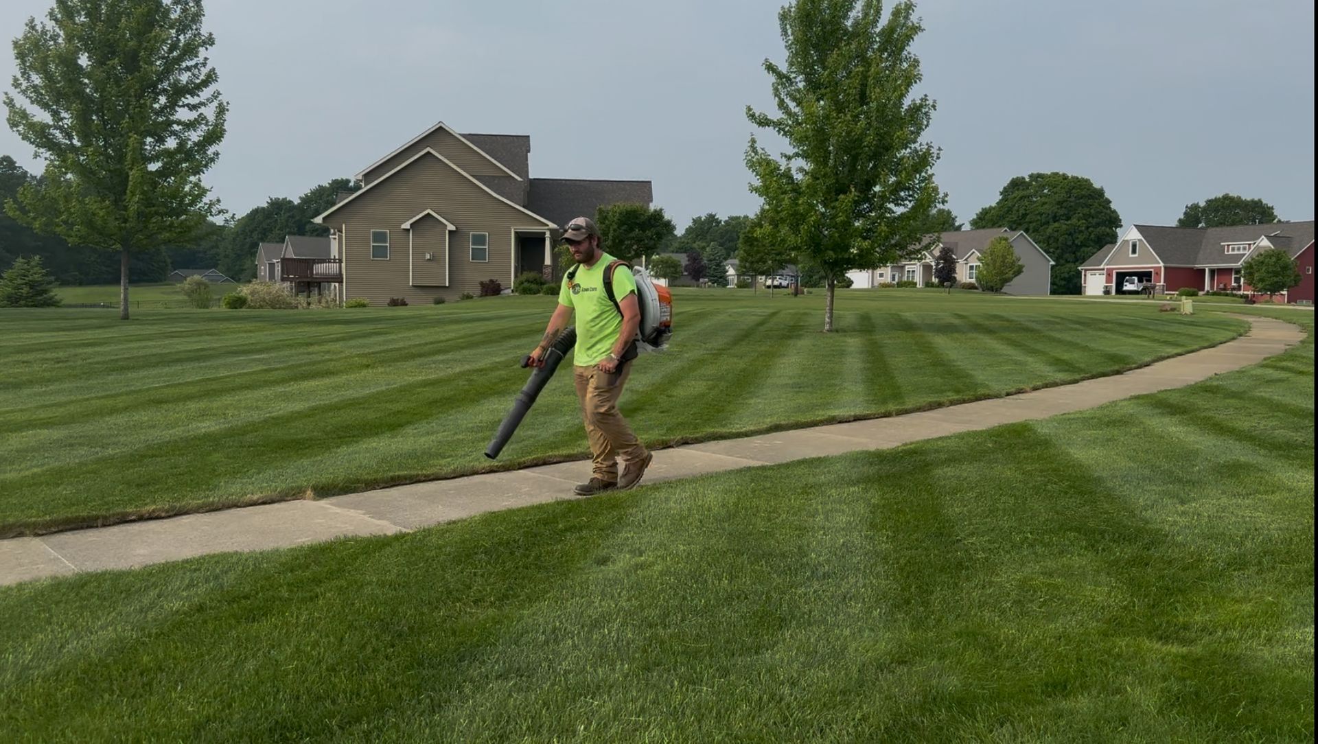 A man is blowing leaves on the side of the road.