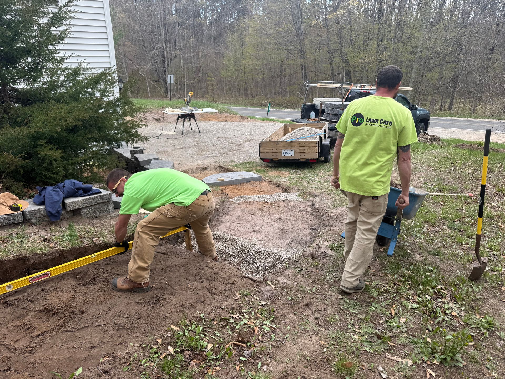 Two workers in neon shirts shovel mud beside a trench at a roadside construction site