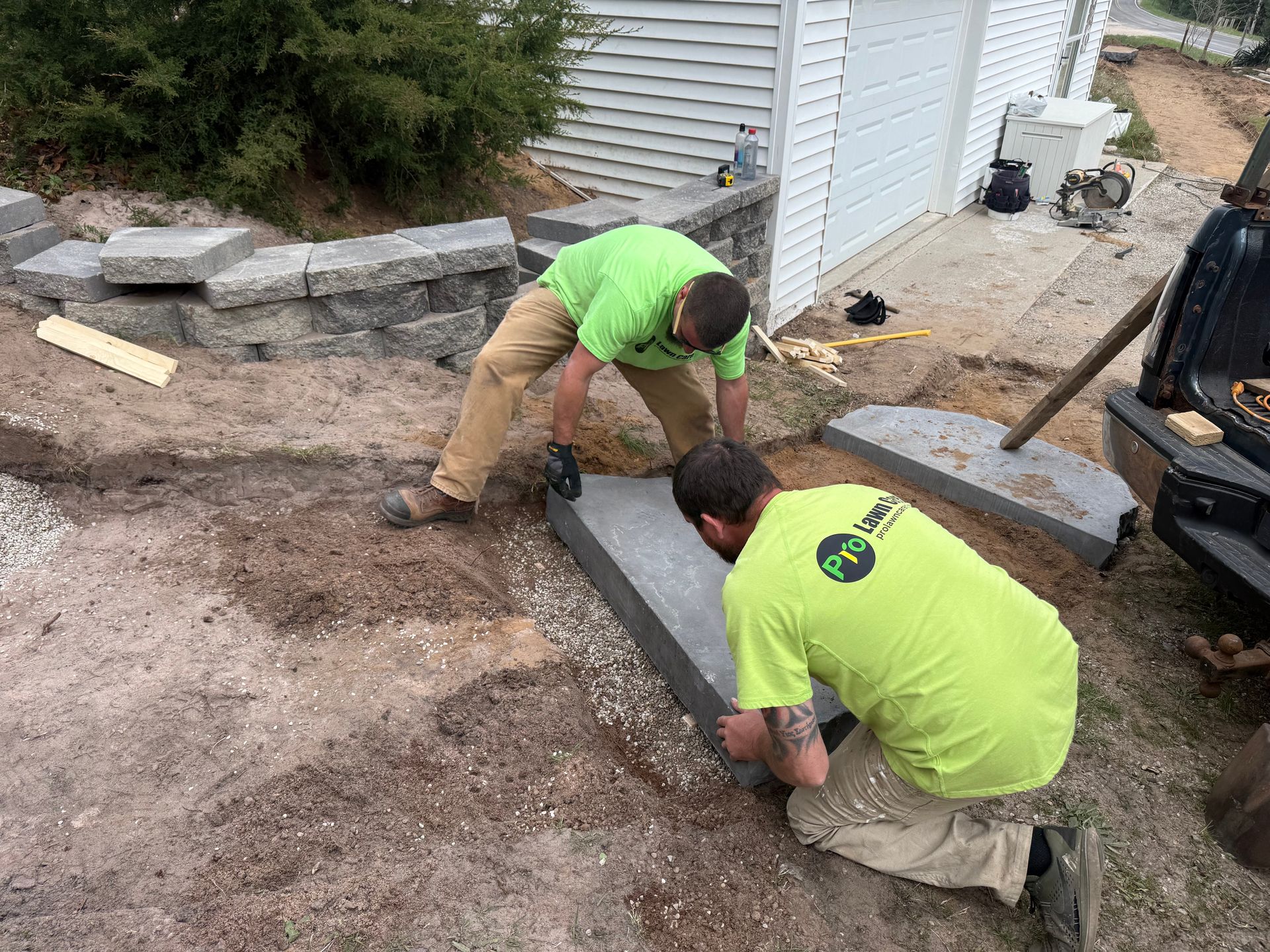 Two workers in neon shirts fitting a concrete step beside a house during construction.