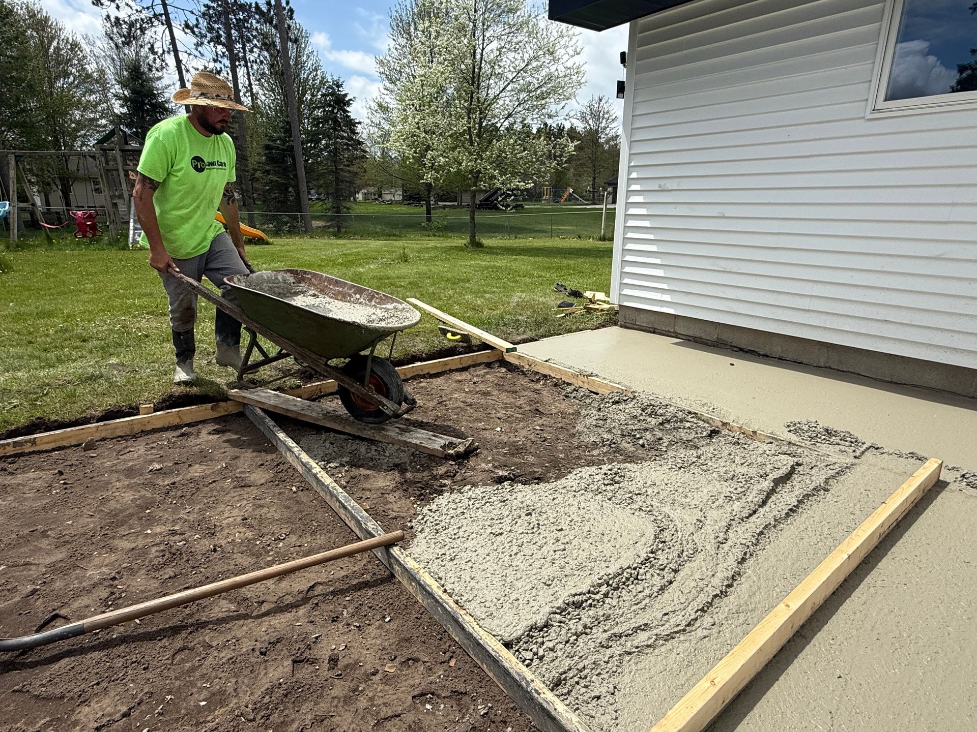 Worker in neon shirt pushing gravel in a wheelbarrow beside a white house during landscaping.