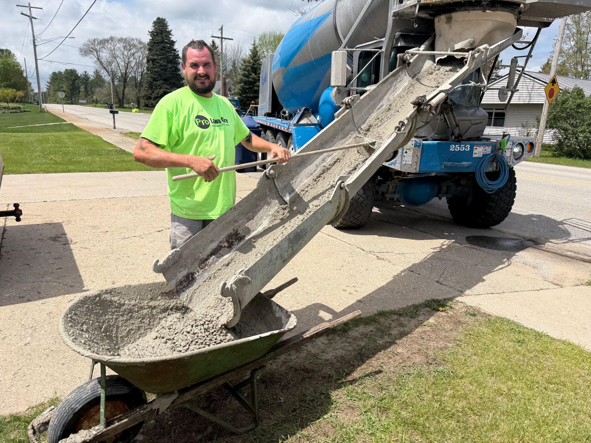 Worker beside concrete mixer chute pouring wet concrete into a wheelbarrow outdoors