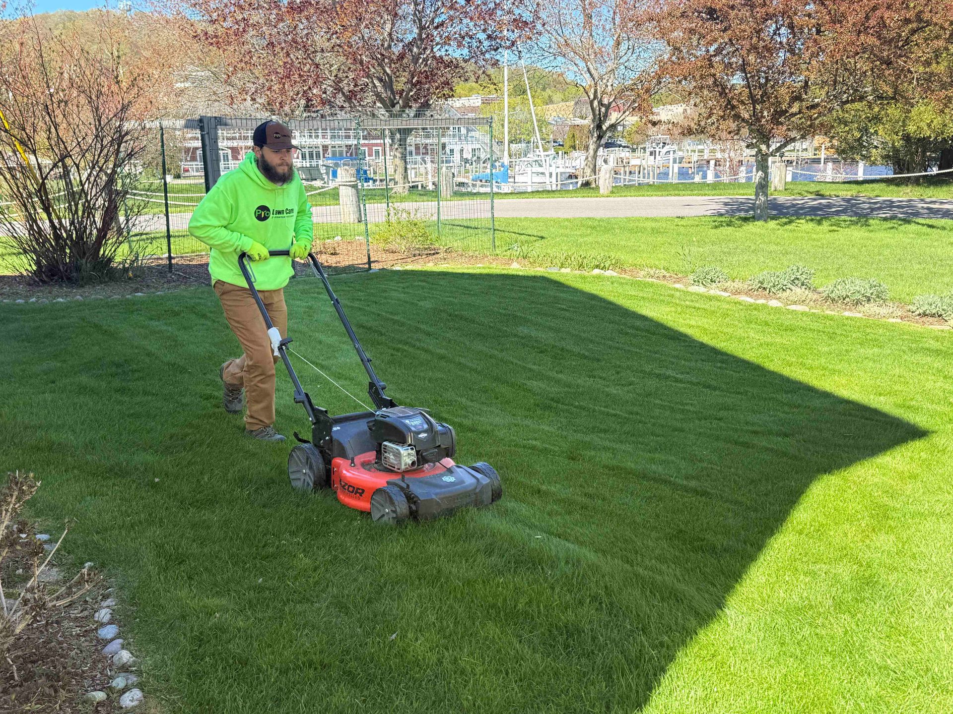 Worker mowing a lawn with an orange push mower beside a house