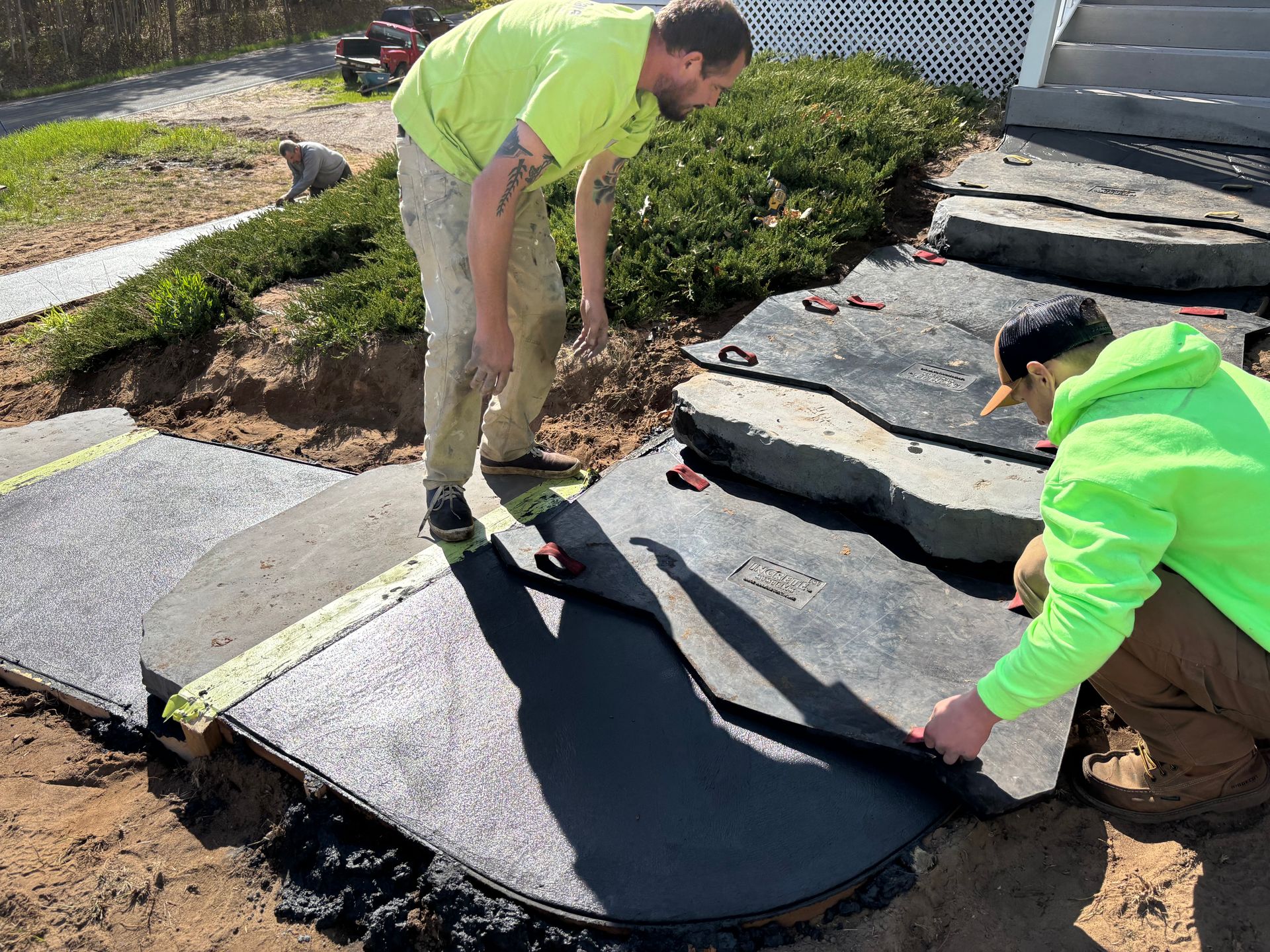 Two workers lifting a large black mat over uneven stone steps in a landscaped yard