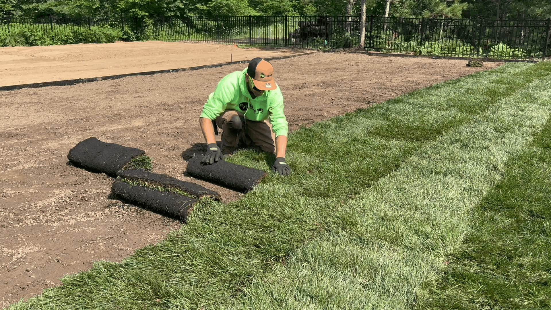 A roll of turf is being laid on top of a pile of dirt next to a rake.