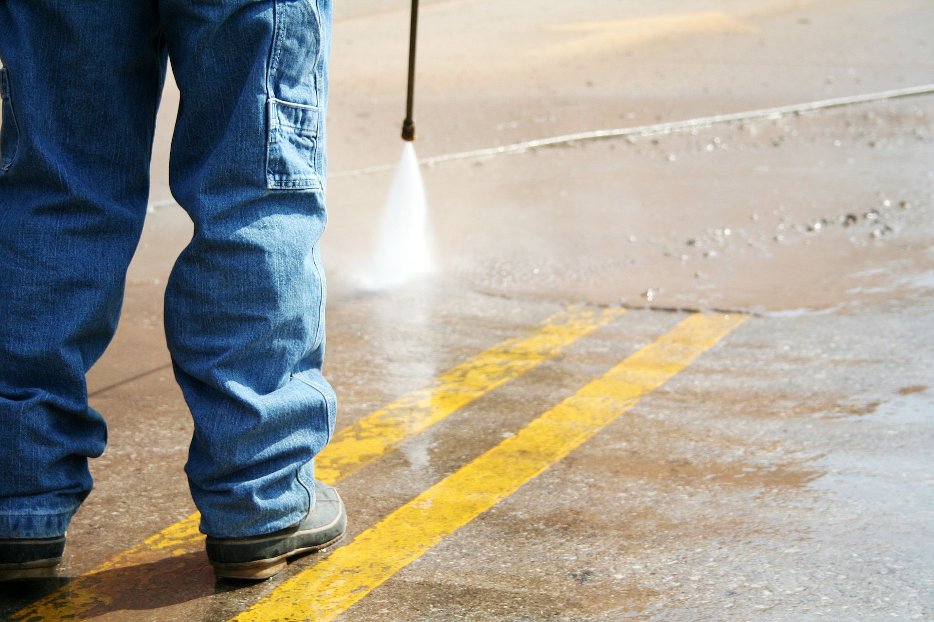A person is using a high pressure washer to clean a parking lot.