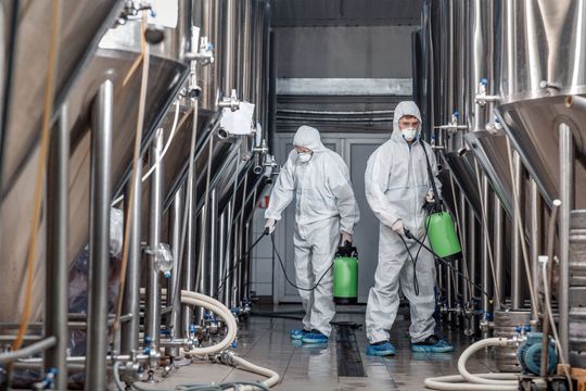 Due operai in tute protettive bianche puliscono serbatoi in acciaio inossidabile in un impianto industriale.