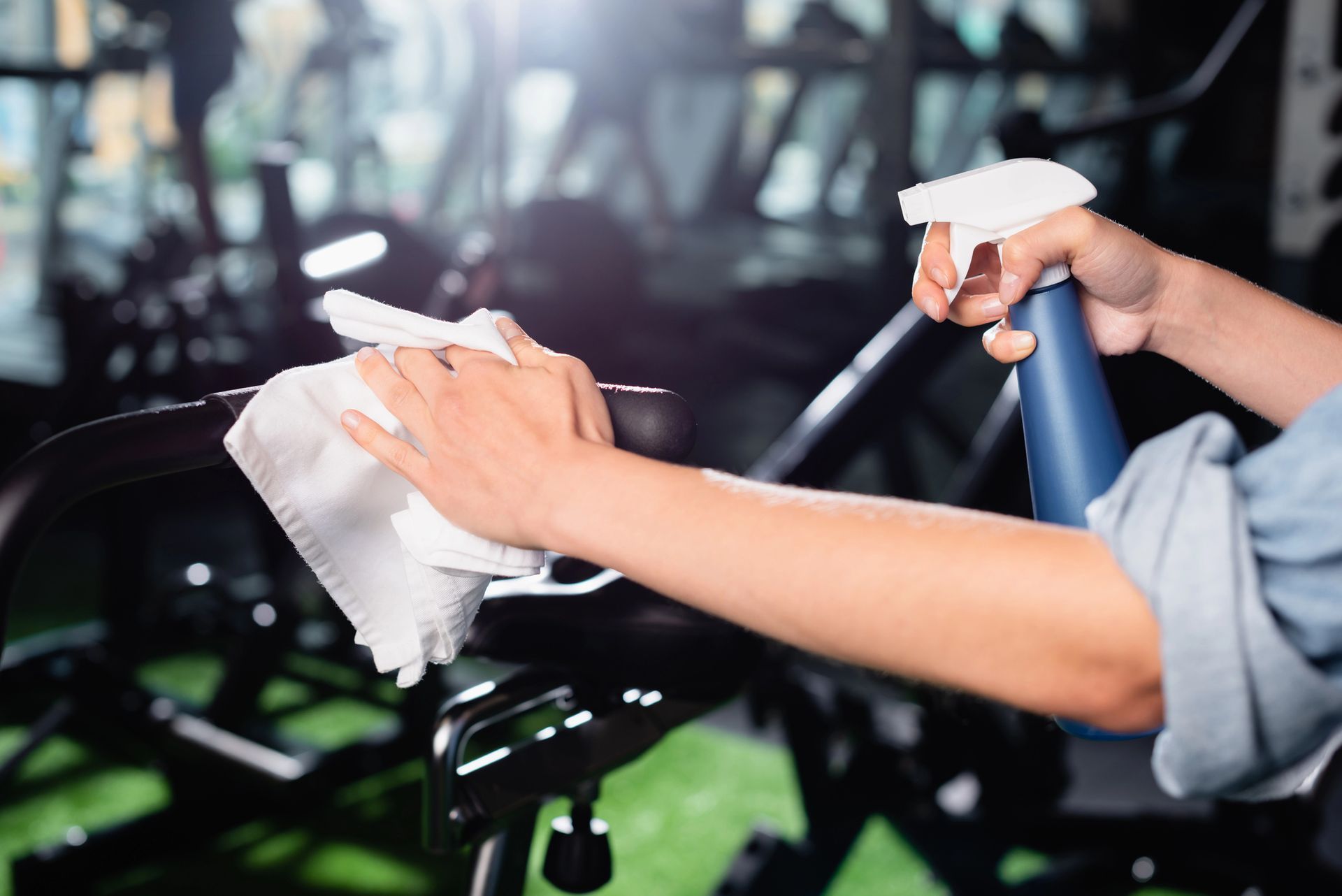 Persona che pulisce le attrezzature della palestra con un panno bianco e un flacone spray.