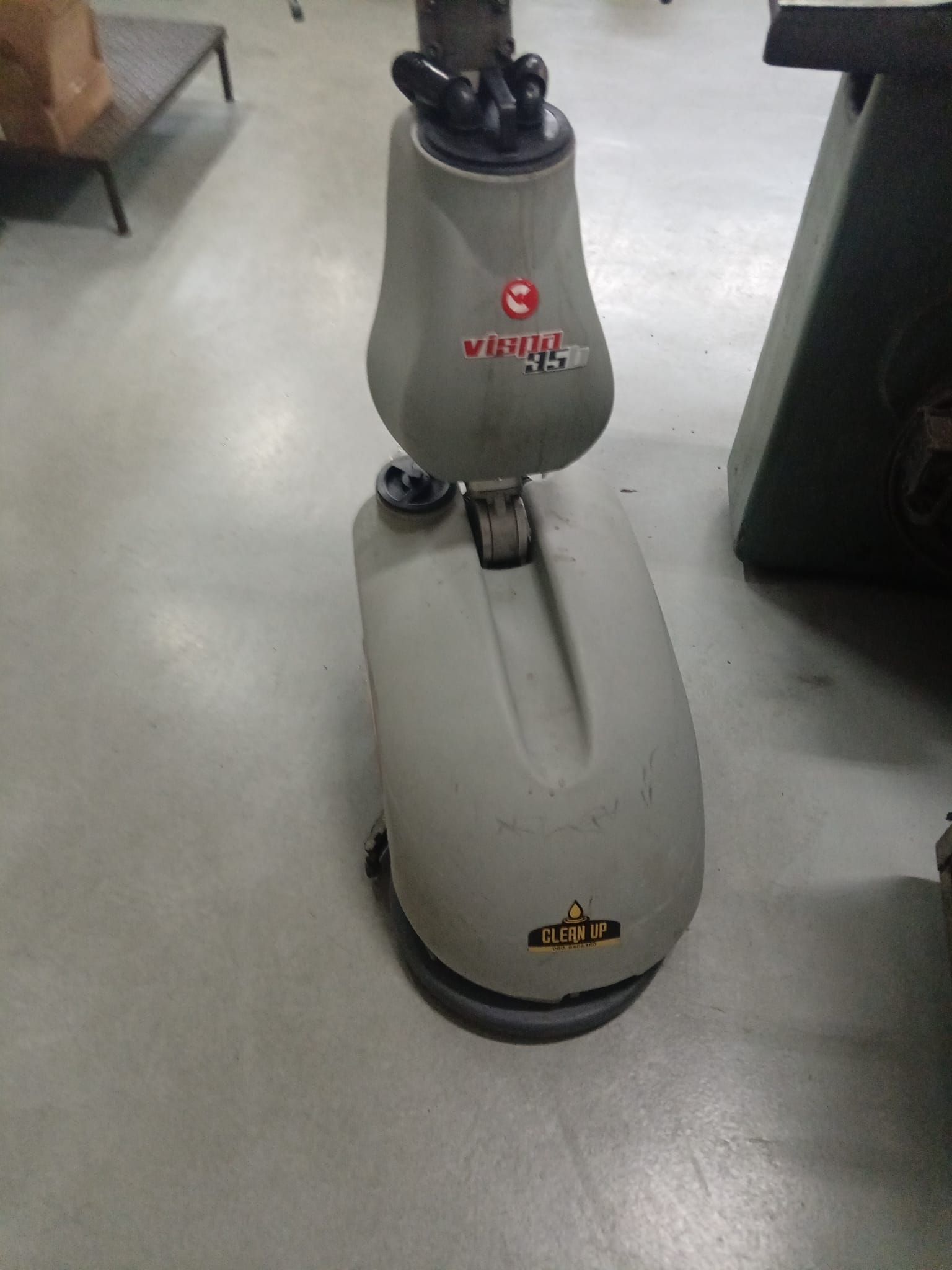 Robot aspirapolvere grigio su un pavimento di cemento in un ambiente interno, con base nera e logo rosso.