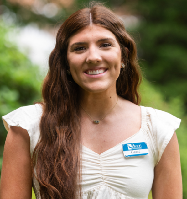 Woman with long brown hair smiles, wearing a patterned blue top, pearl earrings, and a small necklace. Outdoors. - Grace Peters
