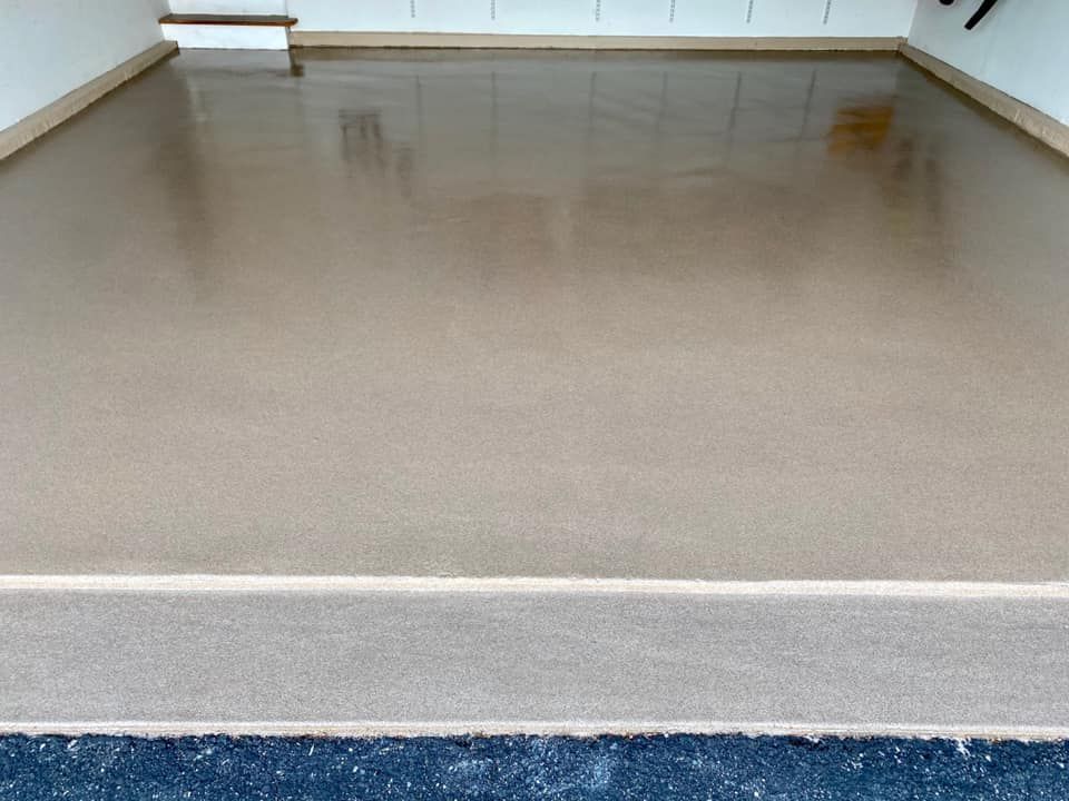 A freshly coated, smooth, light-tan garage floor with a glossy finish meeting a concrete threshold and dark driveway.