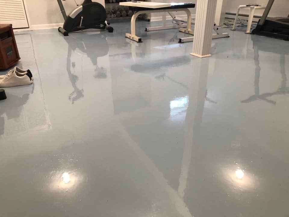 A room with a polished, light-blue epoxy floor, gym equipment, and a white support column in a residential basement.