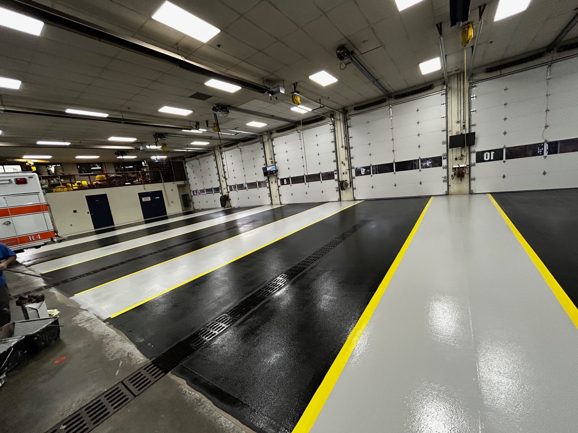 A large, clean garage floor with black and gray epoxy lanes marked by yellow lines, leading toward closed bay doors.