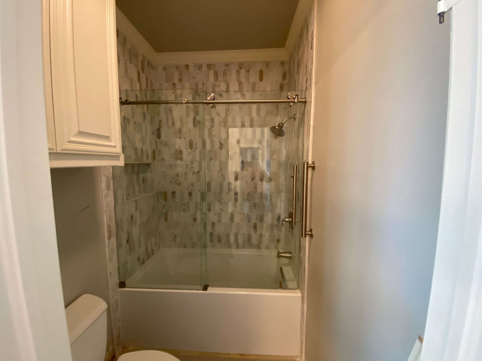 A bathroom with a bathtub, shower, toilet, and cabinets. Gray and white tile wall.
