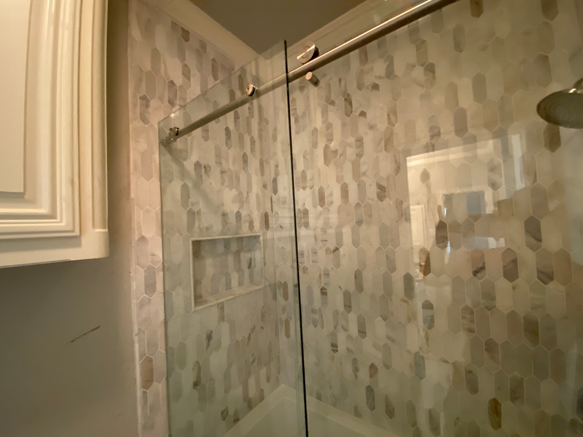 Shower with patterned tile walls, glass door, and built-in shelf.