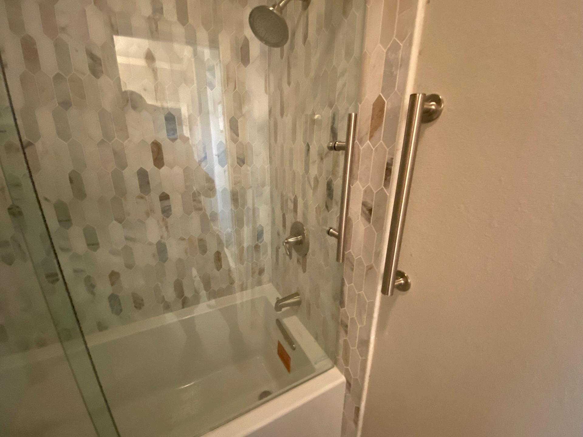 Shower with glass door, hexagon tile, silver fixtures, and a grab bar.
