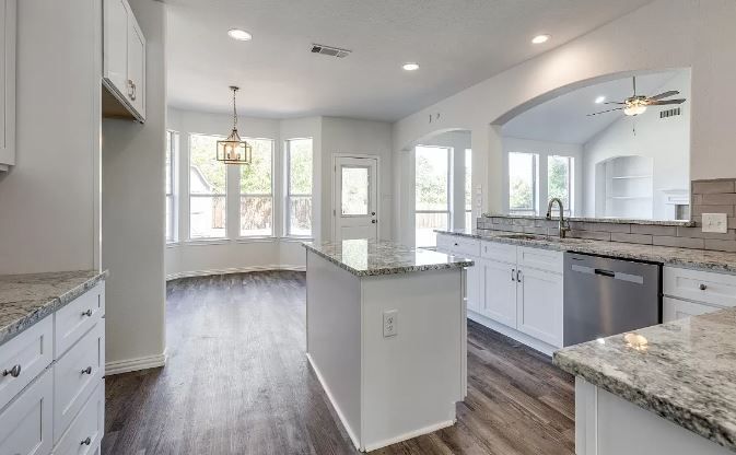 Bright white kitchen with granite countertops, island, and wood-look flooring.