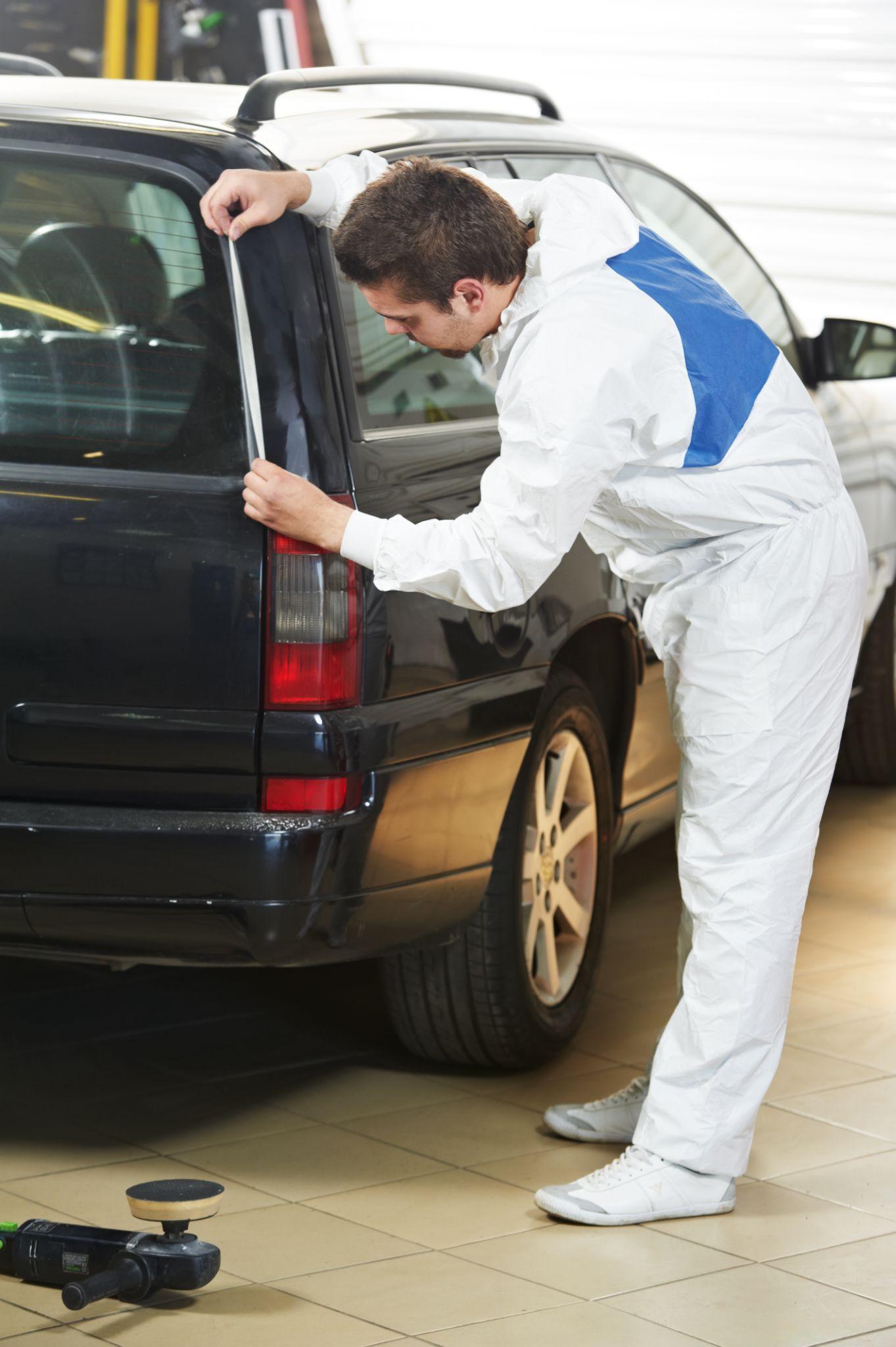 A man in white overalls is working on a car