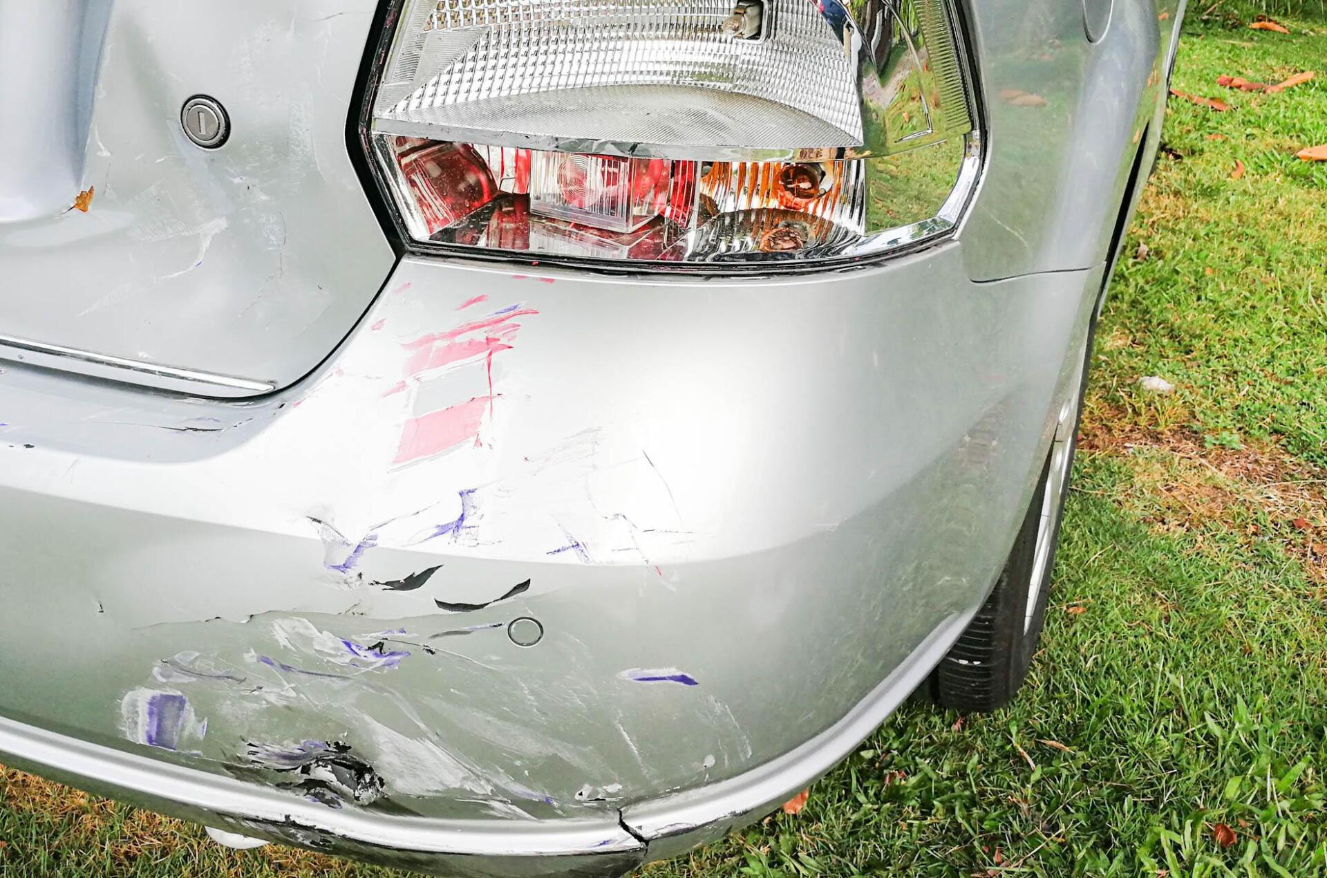 A silver car with a damaged bumper is parked in the grass