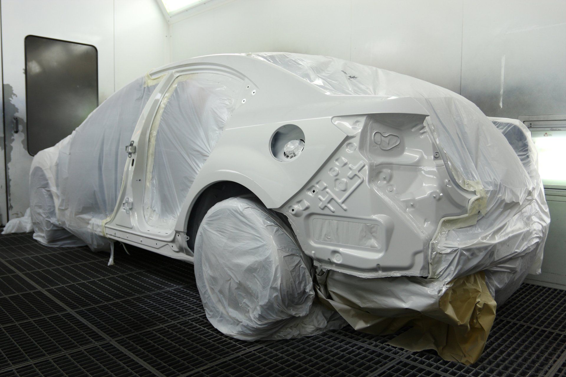 A white car is covered in plastic in a paint booth.