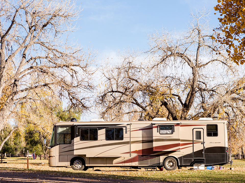 A large rv is parked in a park surrounded by trees